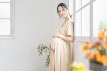 Maternity photoshoot at home. Pregnant woman standing next to window.