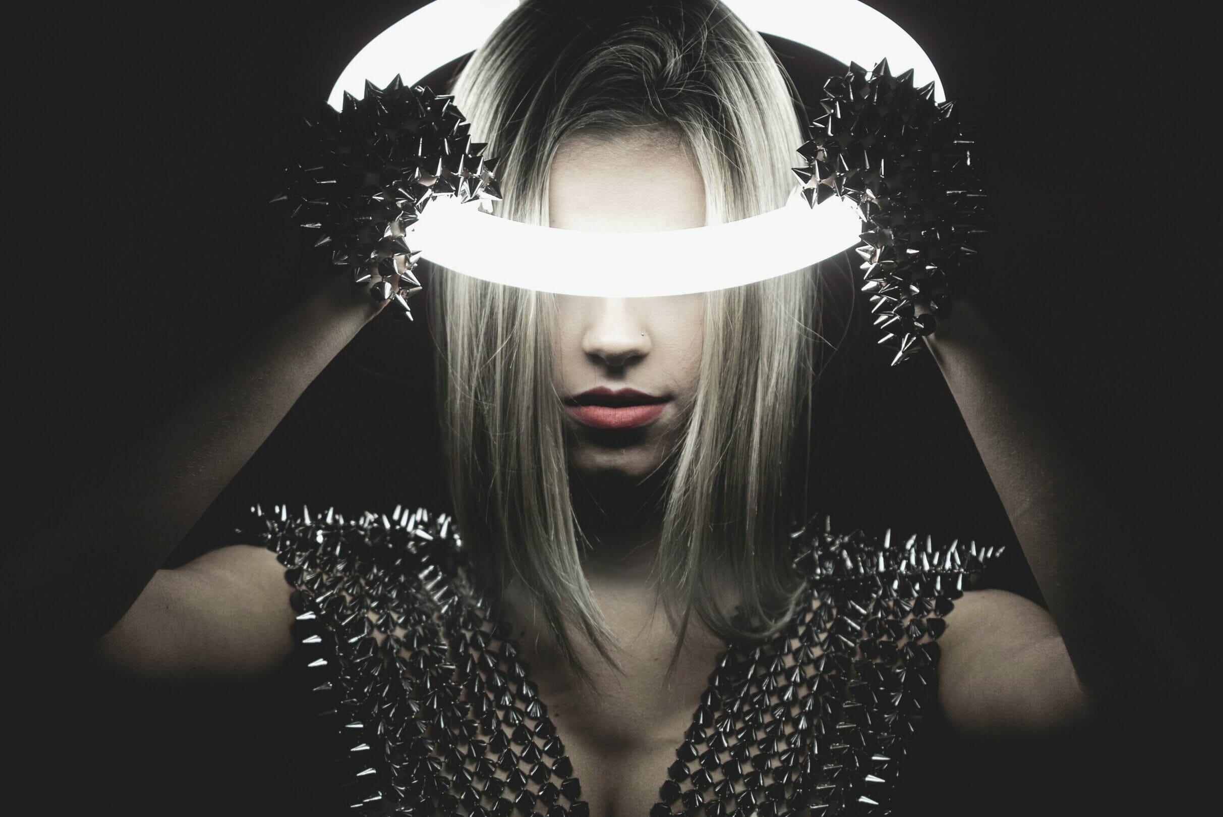 Woman in the dark holding an illuminated neon ring on her head.