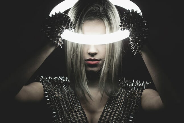 Woman in the dark holding an illuminated neon ring on her head.