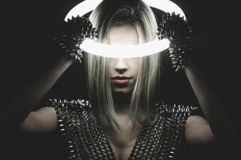 Woman in the dark holding an illuminated neon ring on her head.