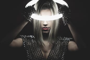 Woman in the dark holding an illuminated neon ring on her head.
