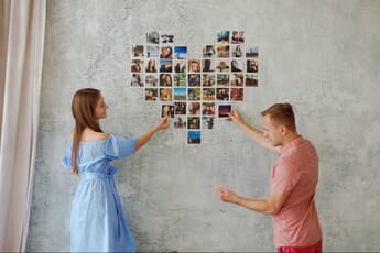 Man and woman creating a heart-shaped wall collage with photo prints