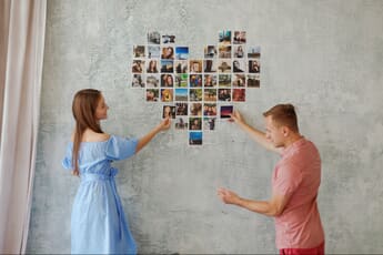 Man and woman creating a heart-shaped wall collage with photo prints
