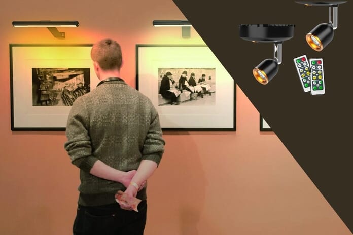 Man looking at pictures at wall a being lit by artificial battery powered LED lights. Picture lights with remote showing in the top-right corner.