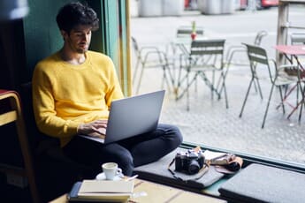 Young Man on a laptop with a camera sitting in a coffee shop.