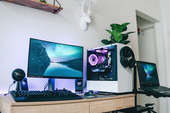 Computer workstation with a desktop computer, headphones, and a plant against a white wall.