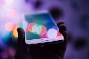 Hand holding smartphone with lights in the background