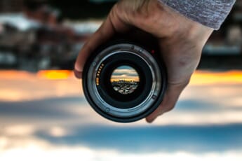 A hand holding a lens with a tiny city at sunset displaying in the glass element.