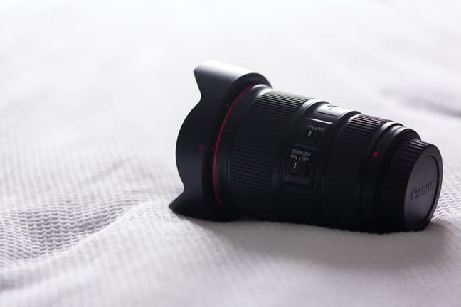 Black Canon lens with focusing and stabilizer switches visible sitting on a white blanket.