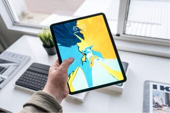 Hand holding out a tablet with a lock-screen abstract photo above a desk.