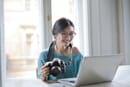 Woman photographer sitting in front of laptop with camera in hand