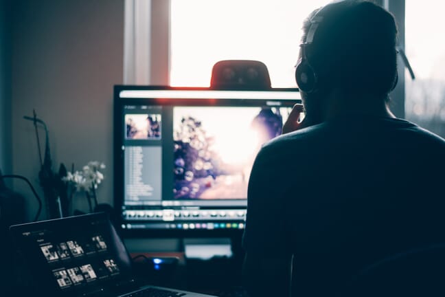 Man sitting in front of a monitor and a laptop while editing photos in Lightroom.