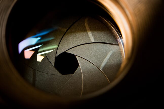 A close-up of a camera lens and aperture blades with colorful reflections.
