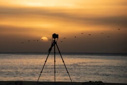 Tripod and camera silhouette overlooking the ocean at sunset.