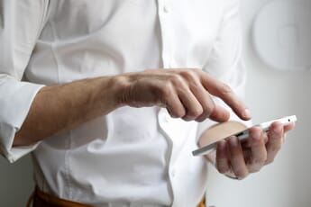 Person wearing a white button-down shirt tapping on the screen of their white phone.