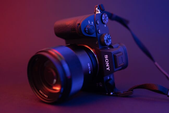 Sony a7 III mirrorless camera with a small lens lying on its side lit by red and blue light.