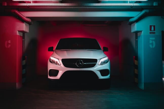 White Mercedes SUV parked in an underground garage with colored blue and red lighting.