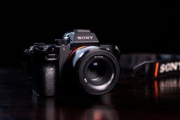 Close-up of a black Sony full-frame mirrorless camera with a short lens sitting on a dark table against a black background.
