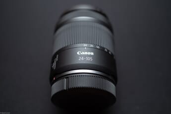 Close-up of a black Canon 24-105mm lens lying on a black surface with the caps on.
