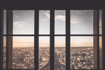 A gridded brown window overlooking a busy city with a warm sunset and wispy clouds.