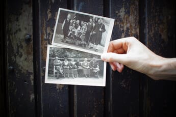 A hand holds out two black and white photo prints in front of a wood background.