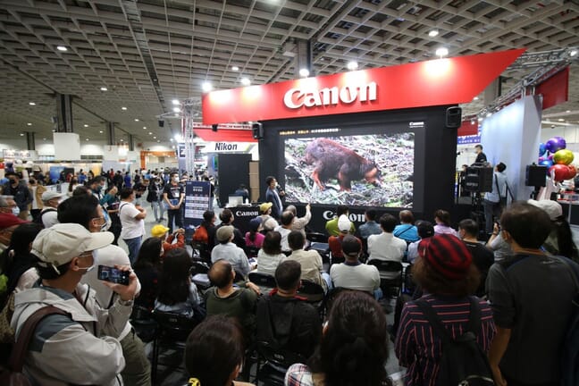 Canon booth at the Taipei Photography & Video Device Exhibition with crowds of people.