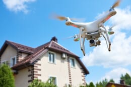 White DJI Phantom drone flying around a house underneath a blue sky.
