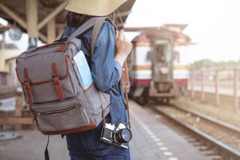 Woman with a camera backpack and a camera on the railway station.