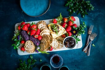 Crackers, cheese, and berries on a white plate above a dark blue surface.