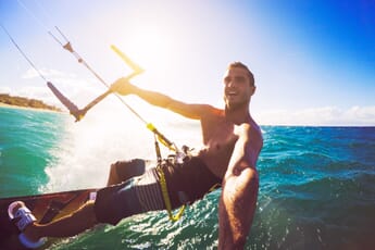 Man kitesurfing on turquoise water while recording with an action camera.