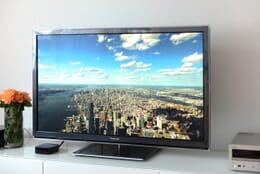 TV displaying a cityscape while positioned on a white surface next to flowers.