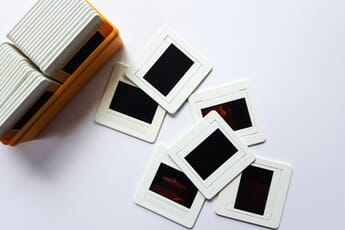 Photo slides spread out on a table next to a box of neatly organized slides.