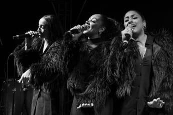 Three singers onstage side by side in black and white.