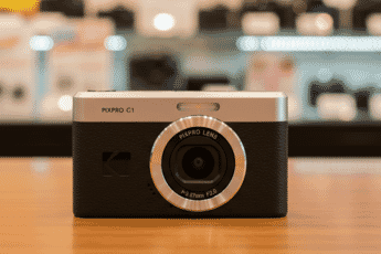 A compact Kodak PIXPRO C1 digital camera with a sleek black and silver design sits on a wooden surface in an electronics store.