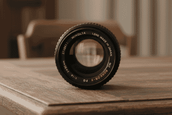 A vintage Minolta Rokkor-X 50mm f/1.4 lens rests on a rustic wooden table, showcasing its classic design and premium craftsmanship.