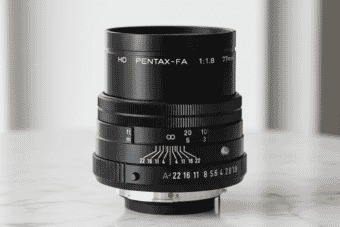 Close-up of the HD Pentax-FA 77mm f/1.8 lens showcasing its sleek black design, manual focus ring, and aperture markings on a marble surface.