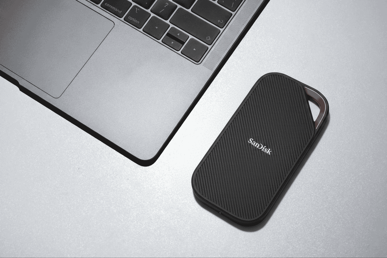 Close-up of a sleek black SanDisk external SSD placed beside a modern laptop on a silver desktop surface.