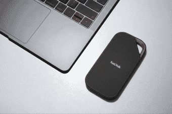 Close-up of a sleek black SanDisk external SSD placed beside a modern laptop on a silver desktop surface.