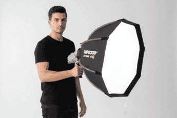 Man in a black t-shirt holding a large octagonal LED softbox light, ideal for professional studio photography and videography lighting setups.