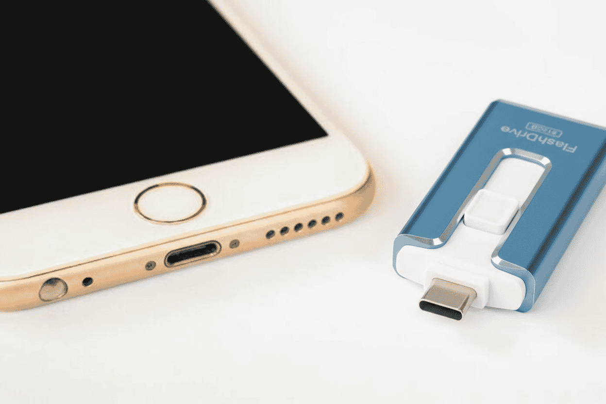 Close-up of a smartphone and a sleek dual-interface USB flash drive with lightning and USB-C connectors on a white surface.