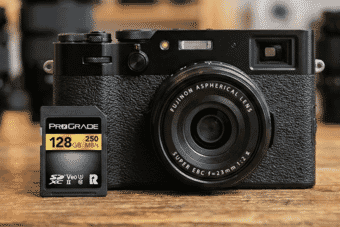 A sleek black Fujifilm mirrorless camera with a 23mm f/2 lens is displayed next to a 128GB ProGrade SDXC memory card on a wooden surface.