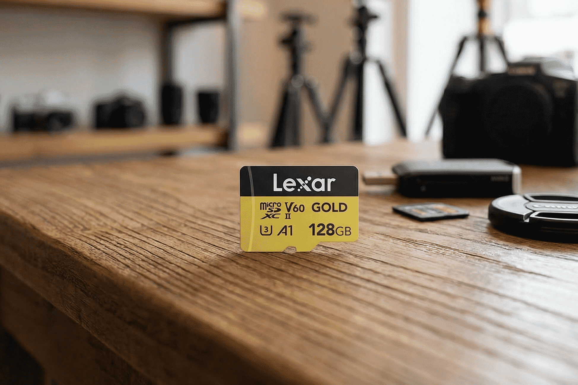A high-performance Lexar 128GB microSD card with V60 speed class stands on a rustic wooden table amid photography gear in a studio setting.