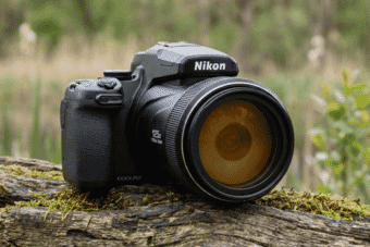 Close-up of a Nikon COOLPIX P1000 digital camera with 125x zoom lens resting on a mossy log in a natural outdoor setting.