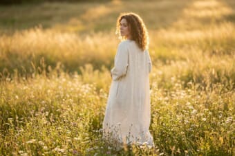 Full body portrait of a woman in a flowing cream dress standing in a golden hour meadow, demonstrating ideal full-body portrait photography techniques
