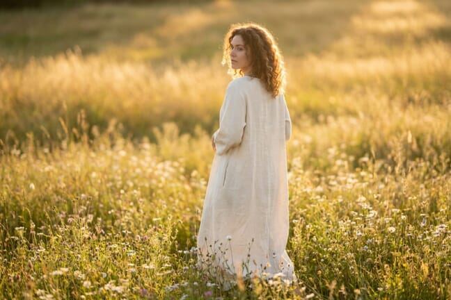 Full body portrait of a woman in a flowing cream dress standing in a golden hour meadow, demonstrating ideal full-body portrait photography techniques
