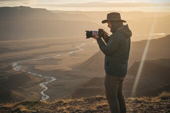 Photographer reviewing photos on camera at golden hour with dramatic landscape behind