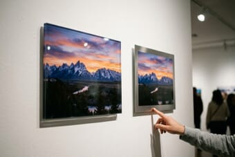 Acrylic print and metal print displayed side by side on a gallery wall showing the same mountain landscape photograph