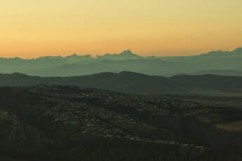 Layered mountain ranges under a golden sunset sky — landscape photography settings guide