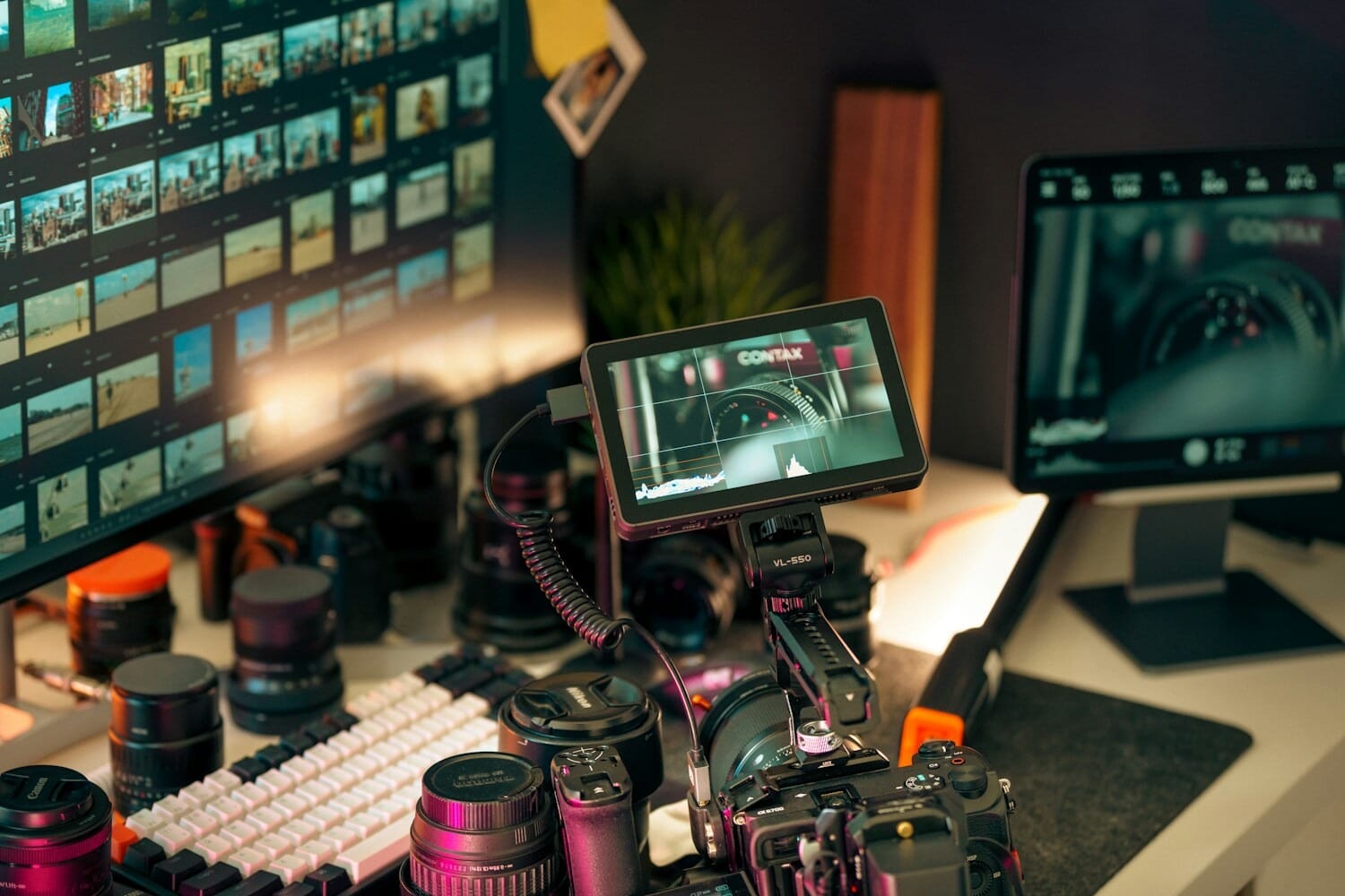 Video editing setup with monitors, camera lenses, and production equipment on a desk
