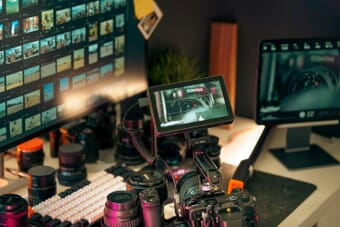 Video editing setup with monitors, camera lenses, and production equipment on a desk